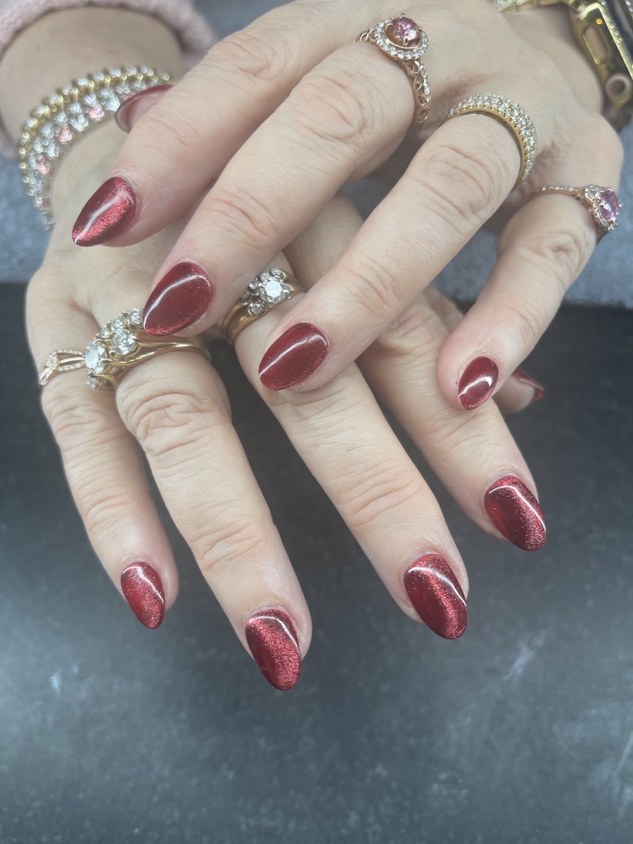 Almond nails in a glossy deep-red cat-eye gel with rings.