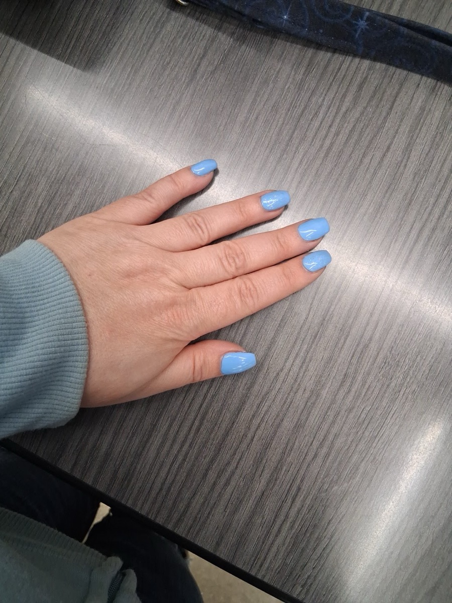 A hand resting on a wood table with soft light-blue almond nails.